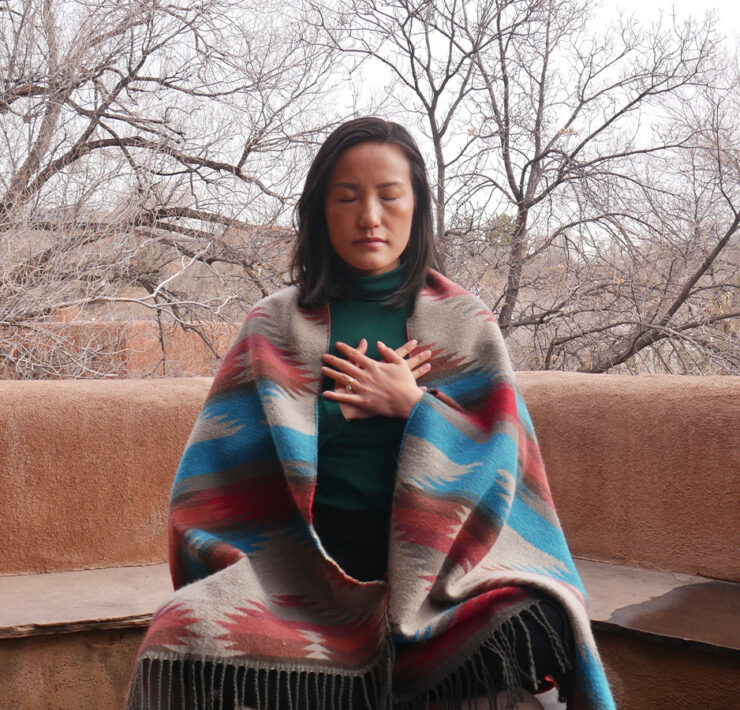 Woman meditating outdoors wearing blanket