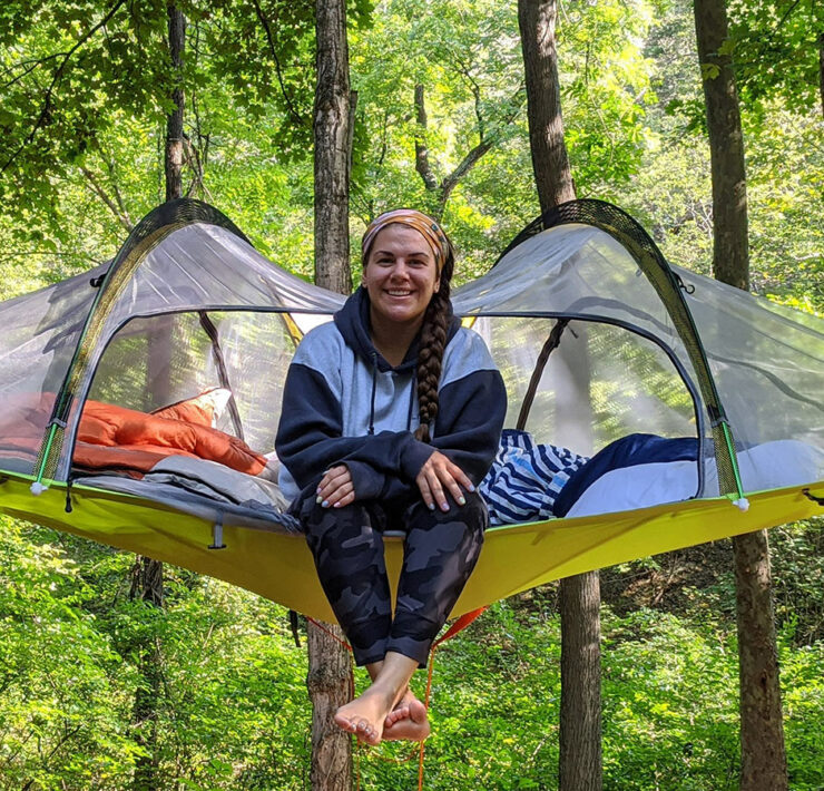 Woman sitting on tent/canopy in the woods