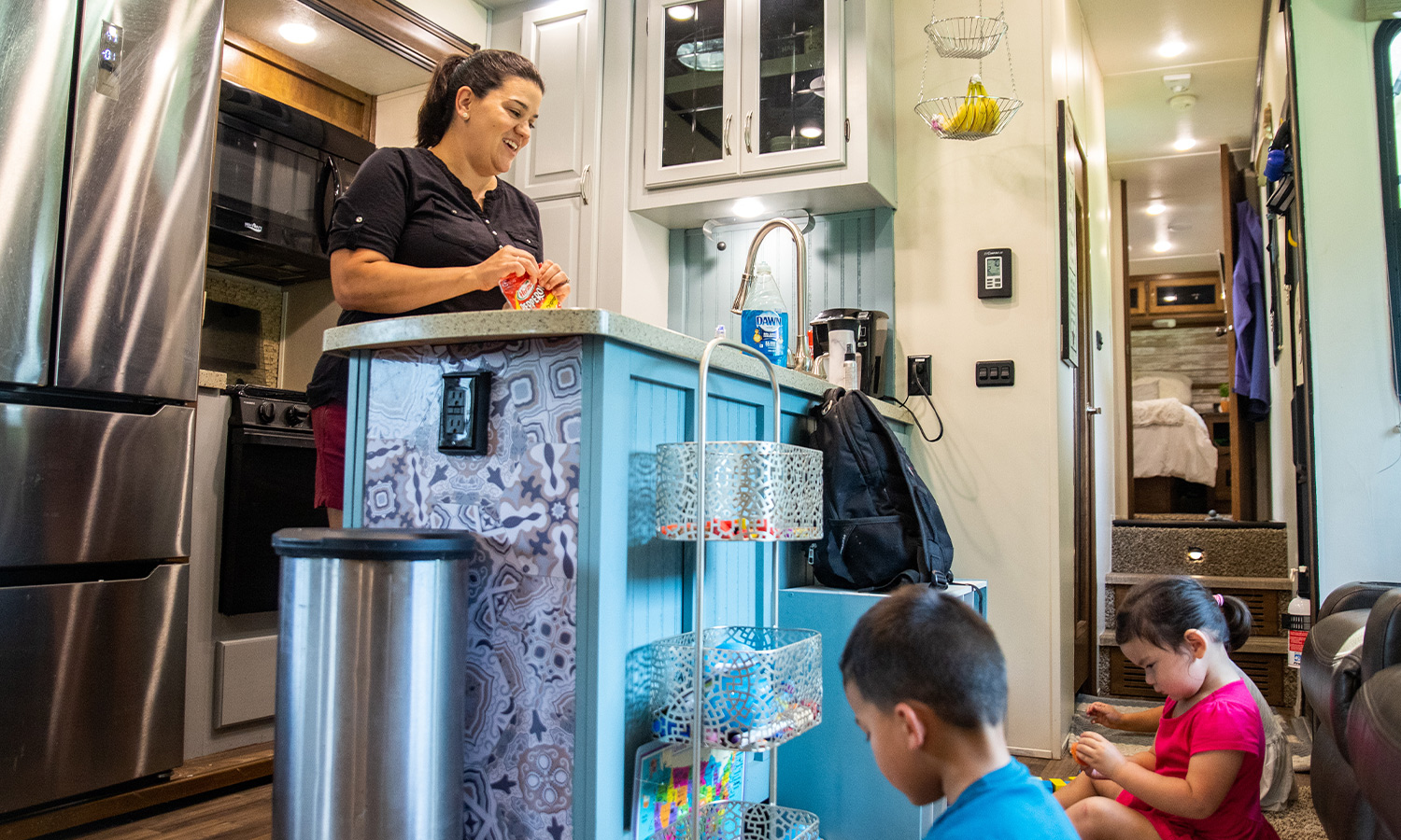 Woman at a kitchen countertop with kids playing with toys on the floor