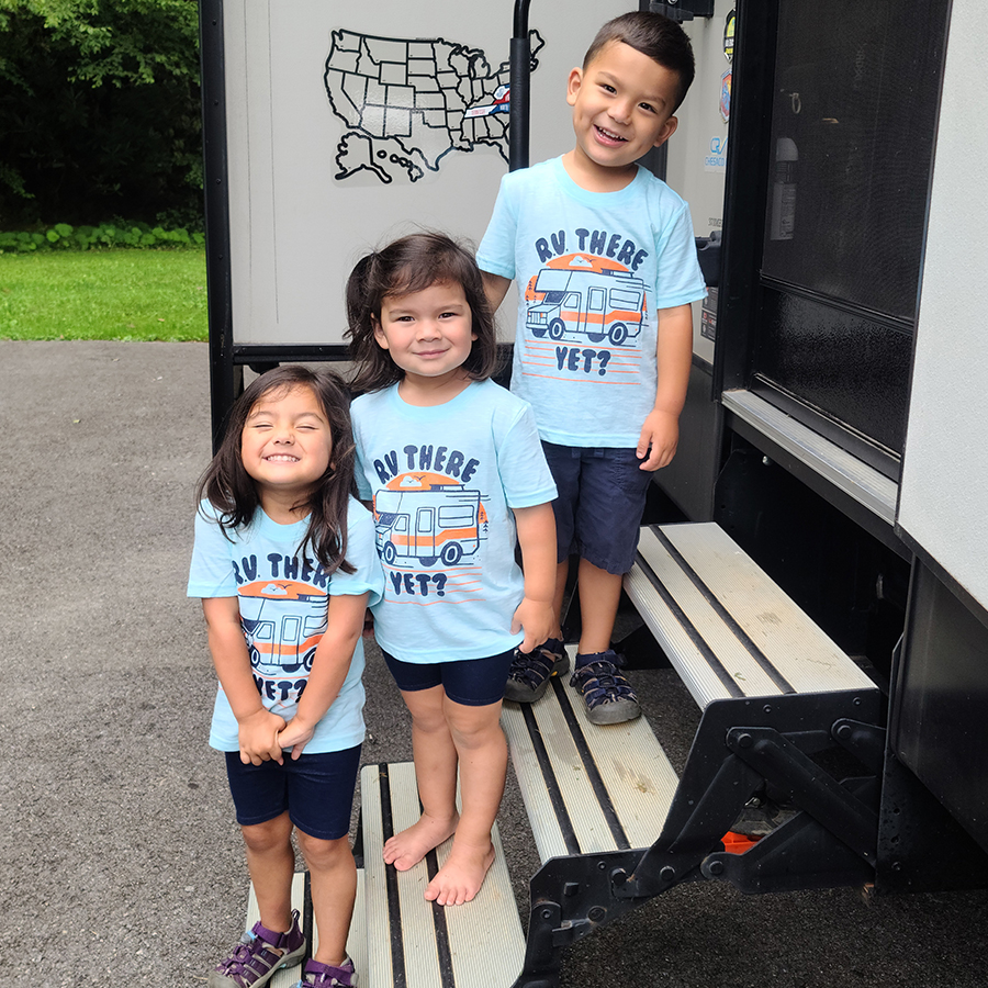 Three children standing on steps smiling in T-Shirts reading "RV There Yet?"