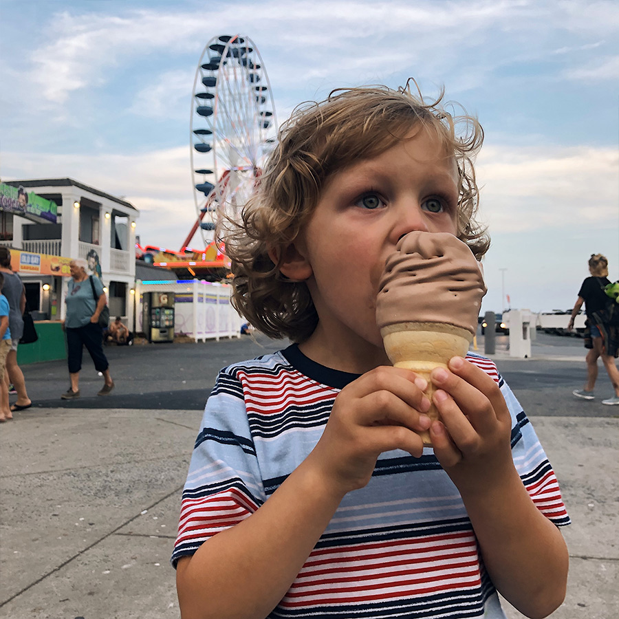 Child eating a chocolate soft serve ice cream cone. Ferris wheel in the background.