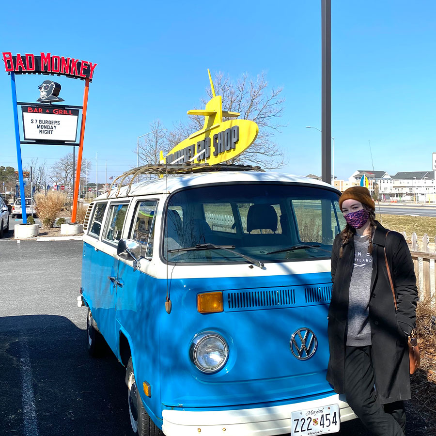 Woman leaning against old VW van in front of the Bad Monkey Sign