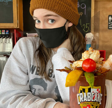Femail wearing a black mask and beanie hat holding her enormous bloody mary beverage