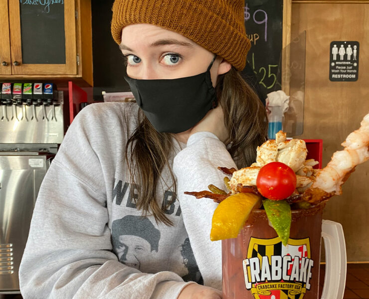 Femail wearing a black mask and beanie hat holding her enormous bloody mary beverage