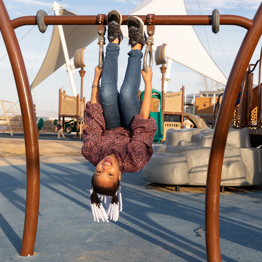 Sailwinds-Girl Girl handing upside down on a jungle gym