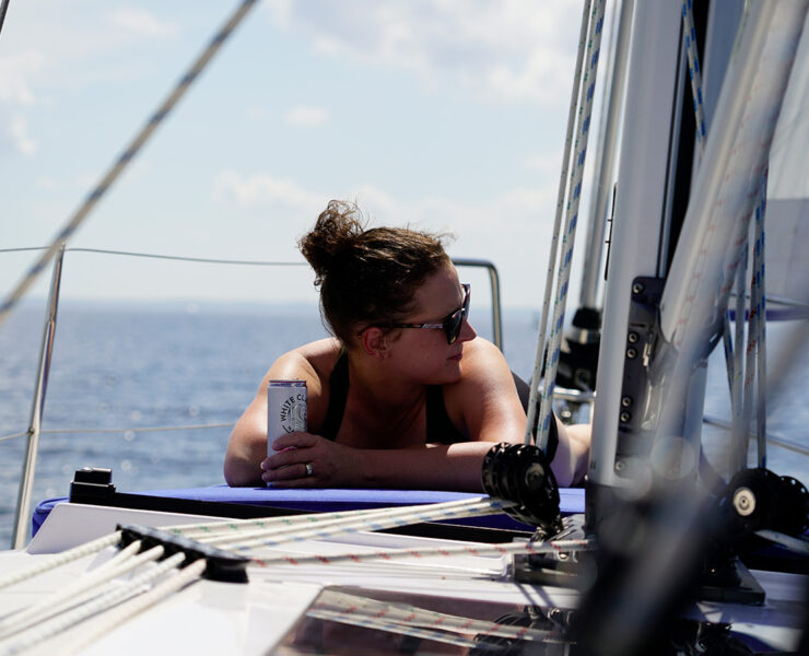 Woman laying on the front of a boat holding a White Claw