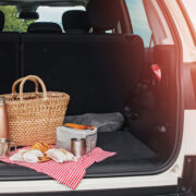 Open trunk door looking into a car with a basket and drinks and food on a cloth