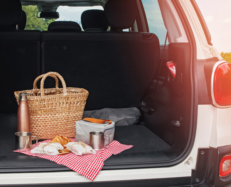 Open trunk door looking into a car with a basket and drinks and food on a cloth