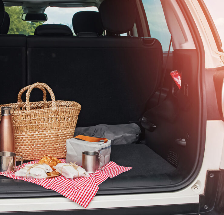 Open trunk door looking into a car with a basket and drinks and food on a cloth