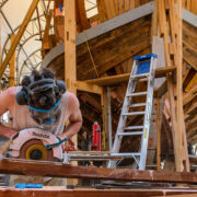A man working with building materials in front of a boat