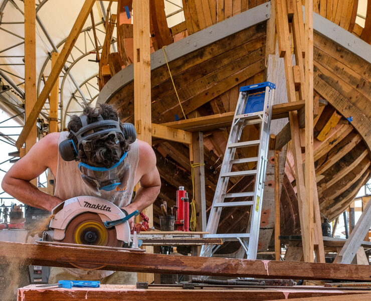 A man working with building materials in front of a boat