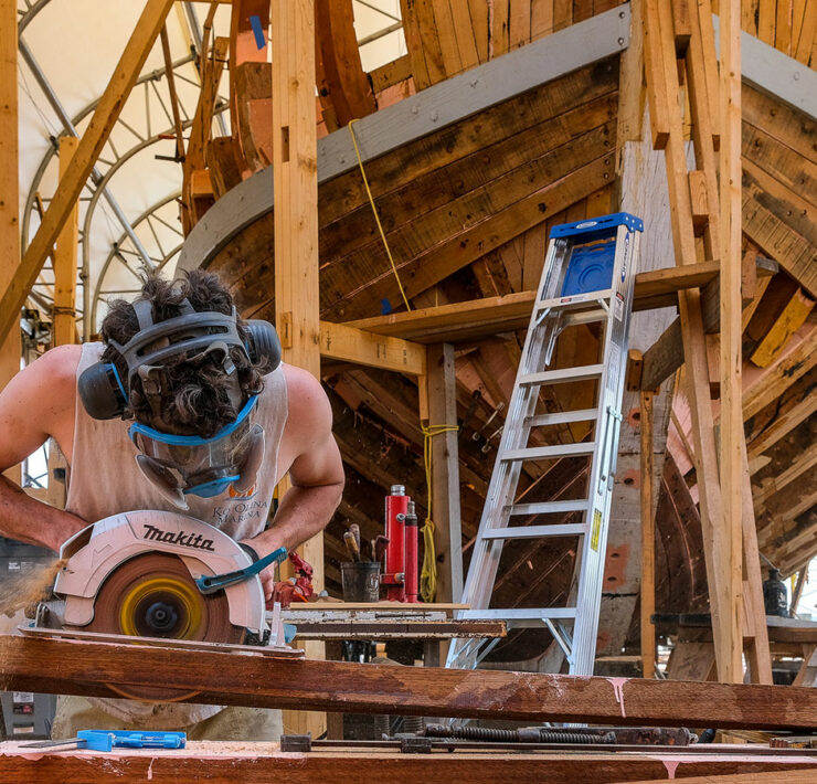 A man working with building materials in front of a boat