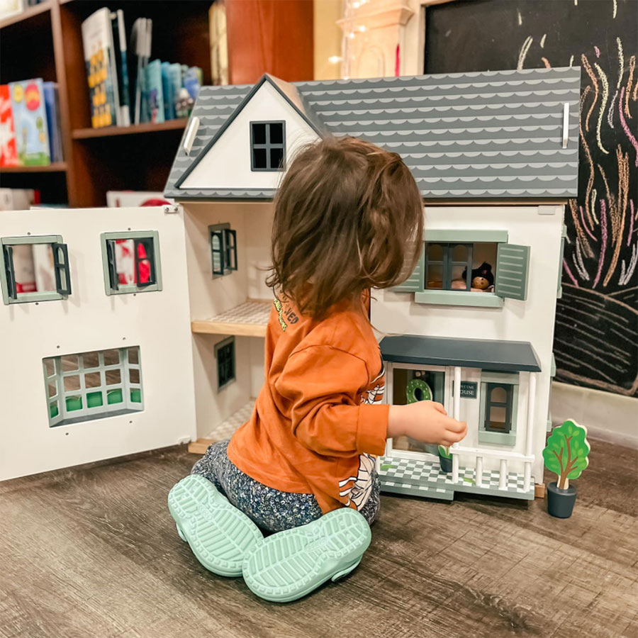 Little girl playing with dollhouse in crocs