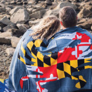 couple sitting on beach wrapped in a Maryland flag towel