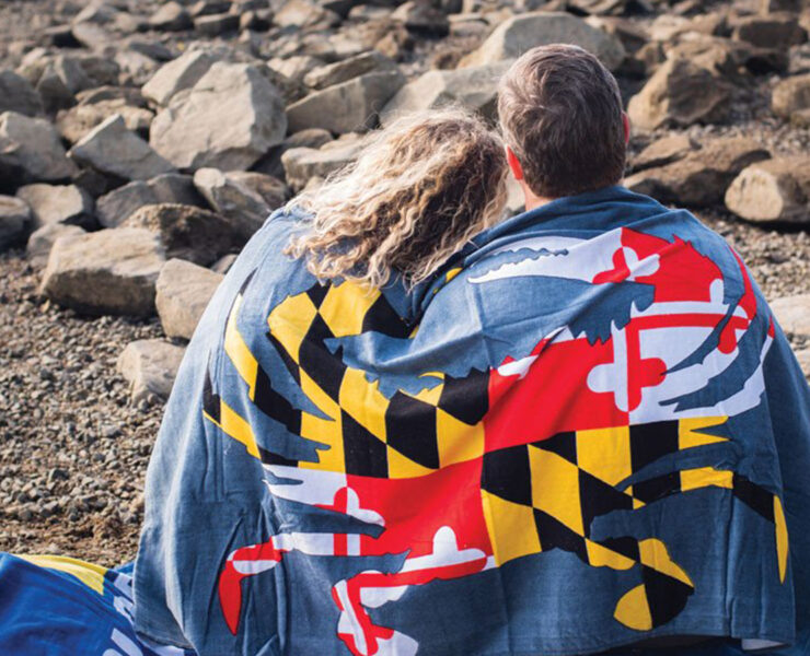 couple sitting on beach wrapped in a Maryland flag towel