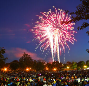A red firework in the night sky above a large group gathered for the show.
