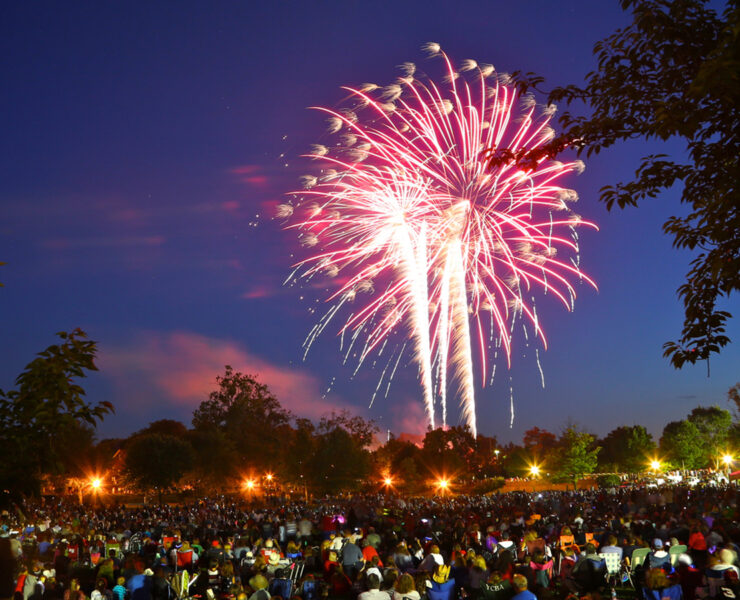 A red firework in the night sky above a large group gathered for the show.
