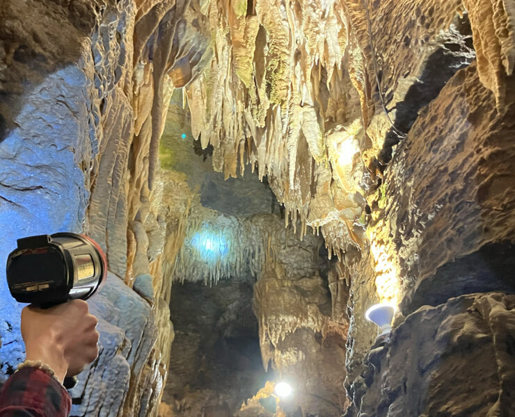 Person holding up handheld spotlight to see amazing cave formations on cave ceiling
