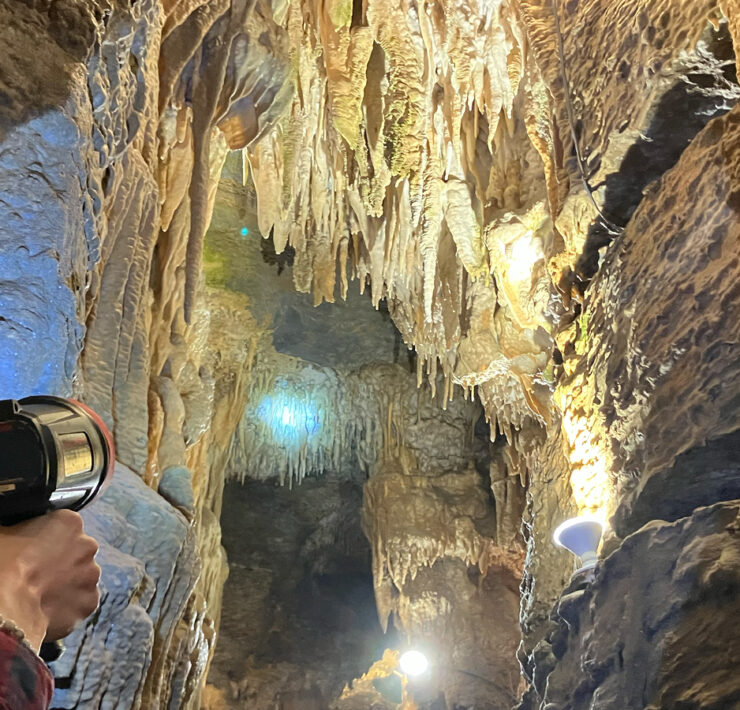 Person holding up handheld spotlight to see amazing cave formations on cave ceiling