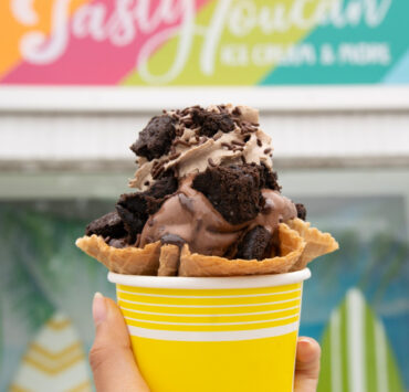 a cup of chocolate ice cream with oreos on it in front of tasty toucan sign