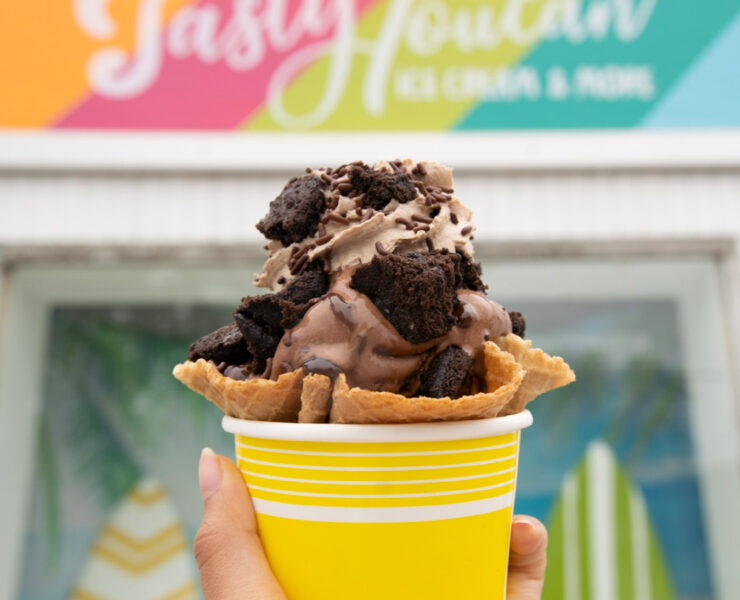 a cup of chocolate ice cream with oreos on it in front of tasty toucan sign