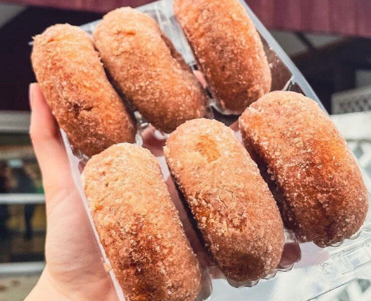 Person holding up a box of cider donuts in front of a barn