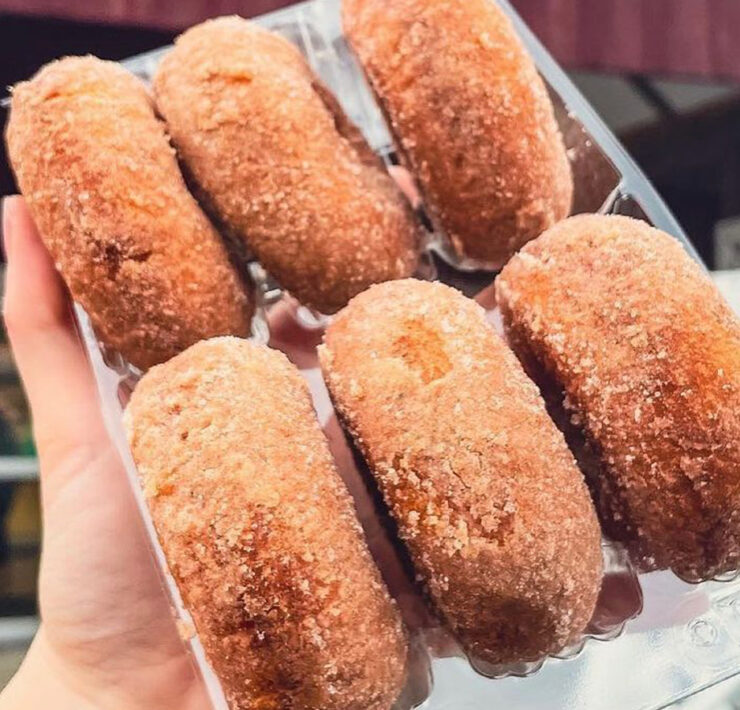 Person holding up a box of cider donuts in front of a barn