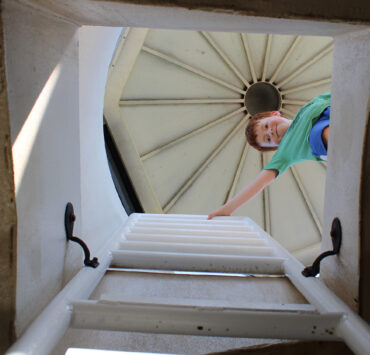 Young boy at the top of a lighthouse looking down the opening and ladder