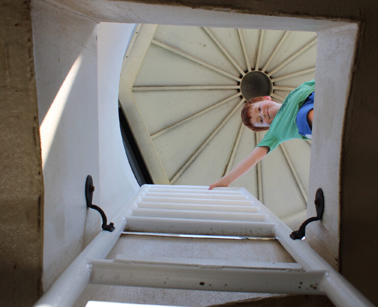 Young boy at the top of a lighthouse looking down the opening and ladder