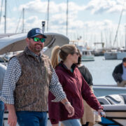 A coupe smiling while walking by boats at a dock