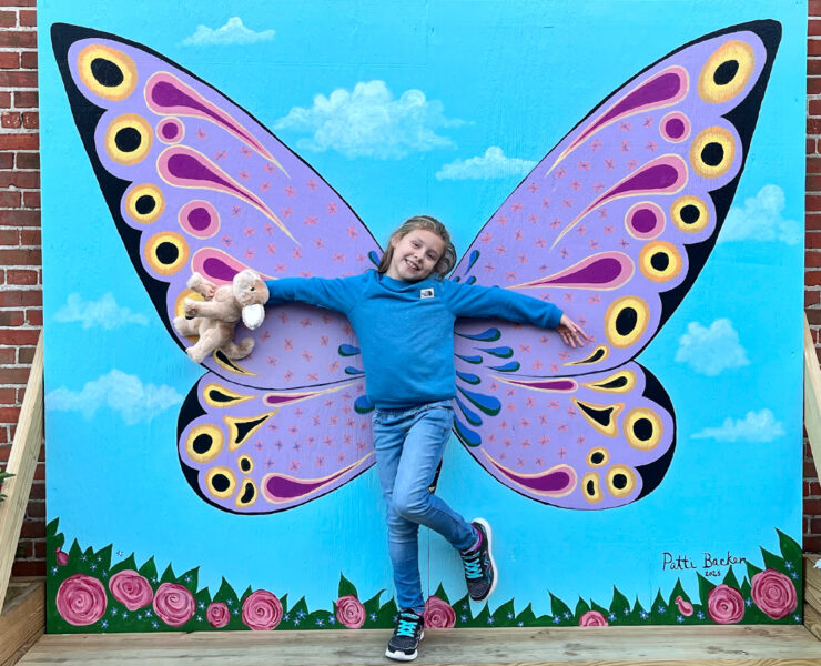 Girl poses in front of butterfly wings mural