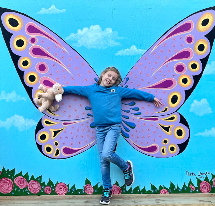 Girl poses in front of butterfly wings mural