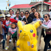 People pose with a giant Pikachu stuff animal on a boardwalk