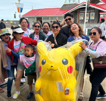 People pose with a giant Pikachu stuff animal on a boardwalk